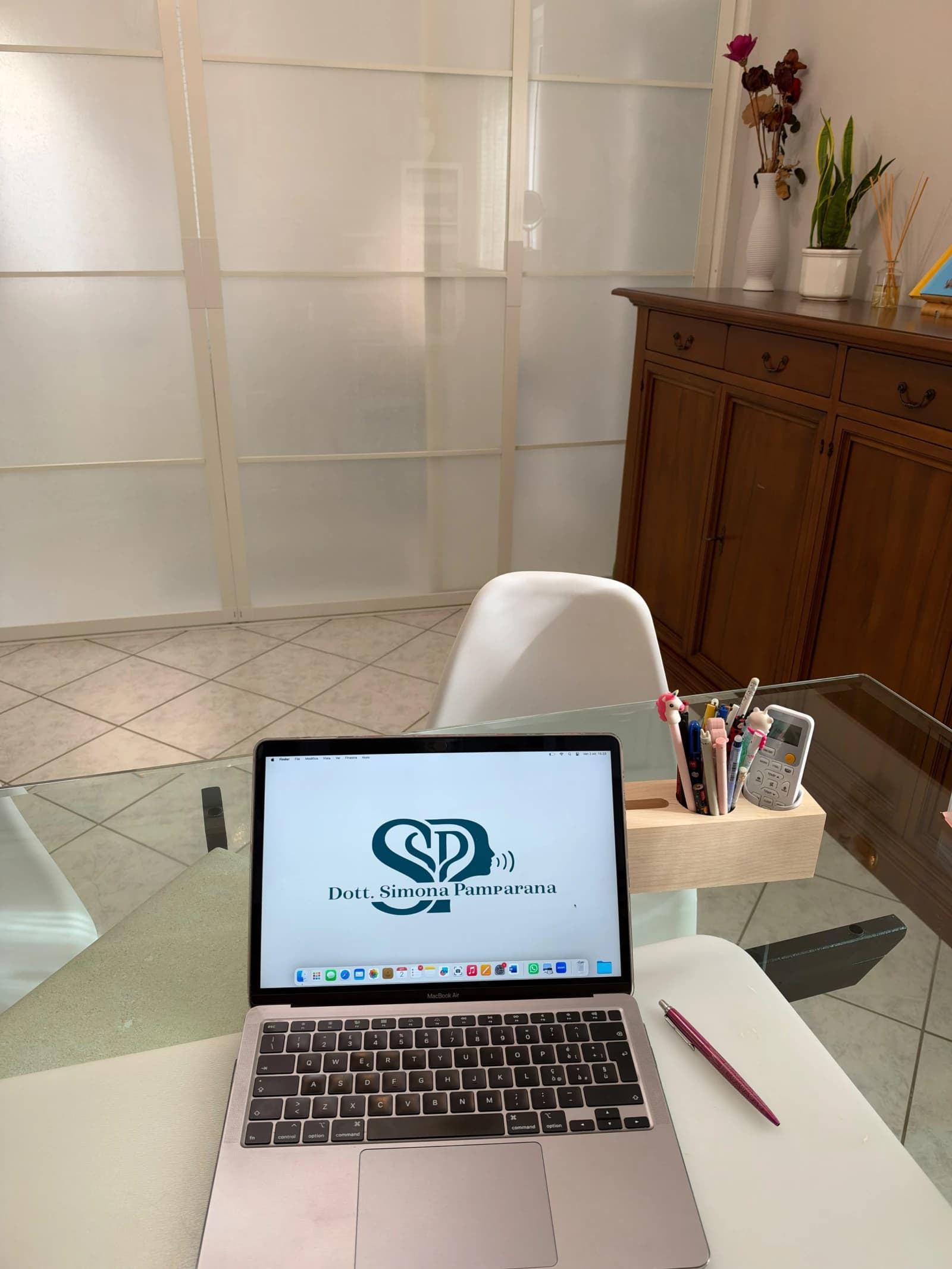 Il portatile con il logo dello studio sulla scrivania di vetro, accanto al portapenne
